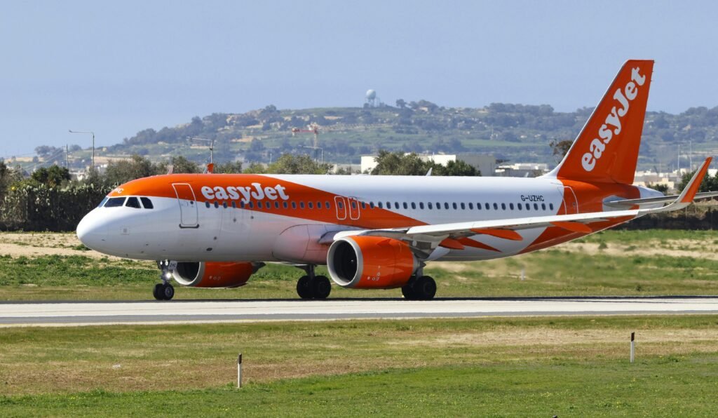 Orange and white easyJet passenger jet on a taxiway with hills in the background beneath a clear sky.