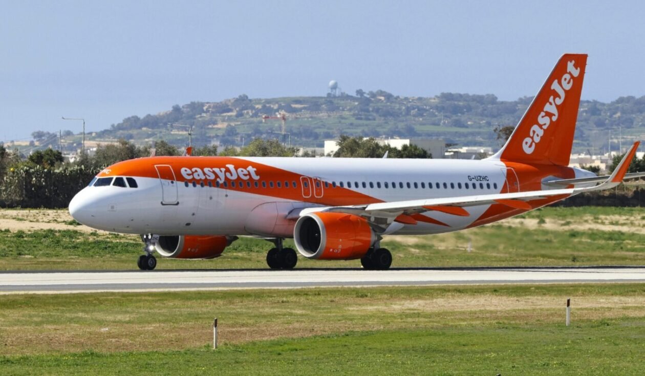 Orange and white easyJet passenger jet on a taxiway with hills in the background beneath a clear sky.