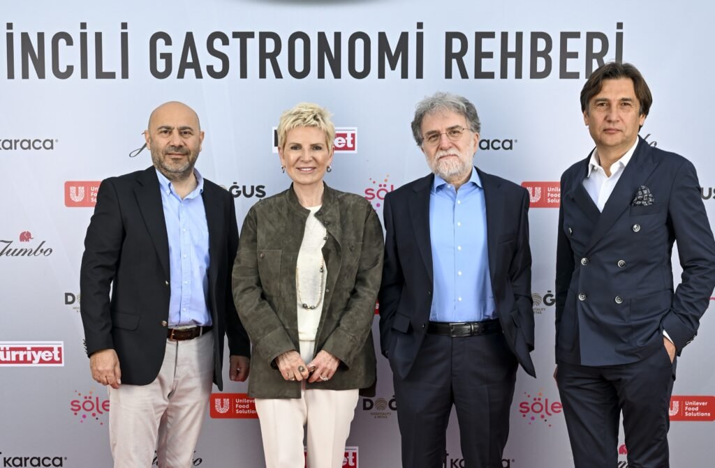 Four professionals posing in front of a backdrop that says 'Gastronomi Rehberi' with sponsor logos visible behind them, medium close-up group shot.