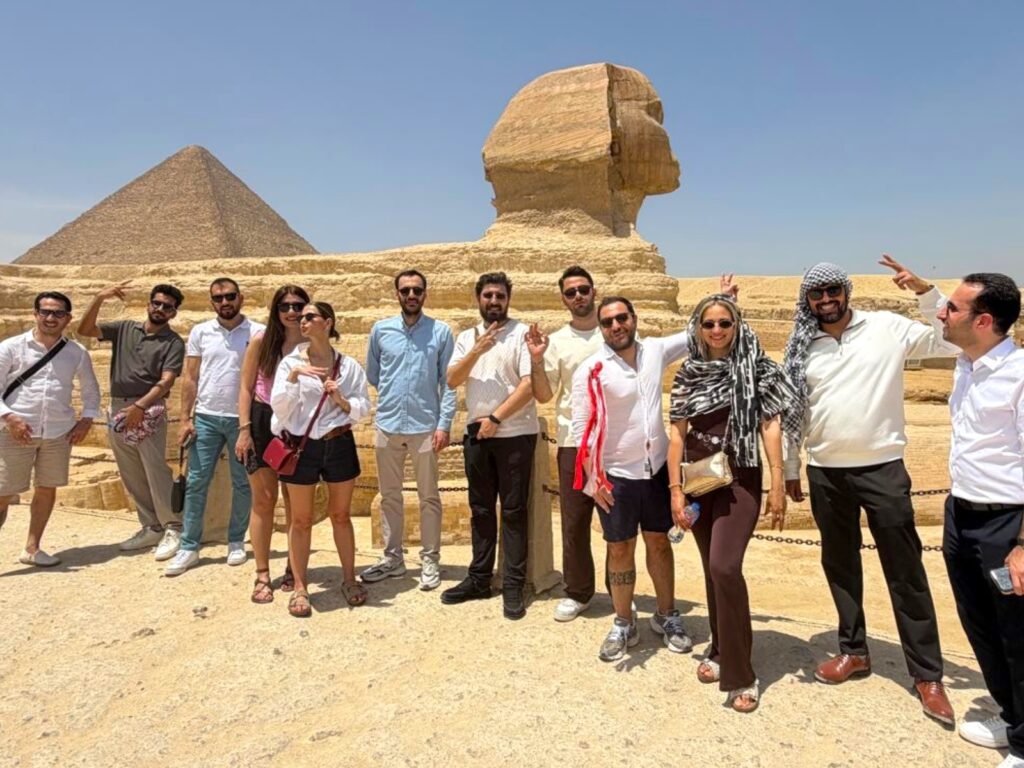 Group of tourists posing in front of the Great Pyramid and the Sphinx on a sunny day in Egypt.