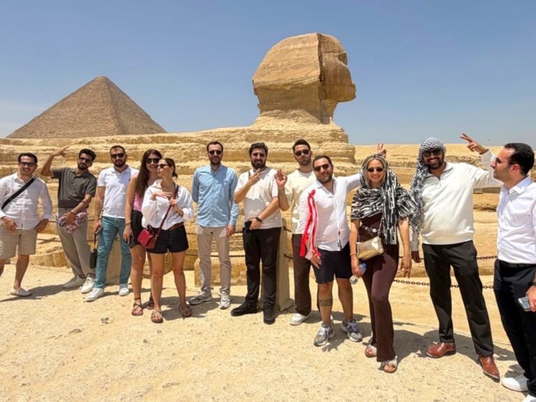 Group of tourists posing in front of the Great Pyramid and the Sphinx on a sunny day in Egypt.