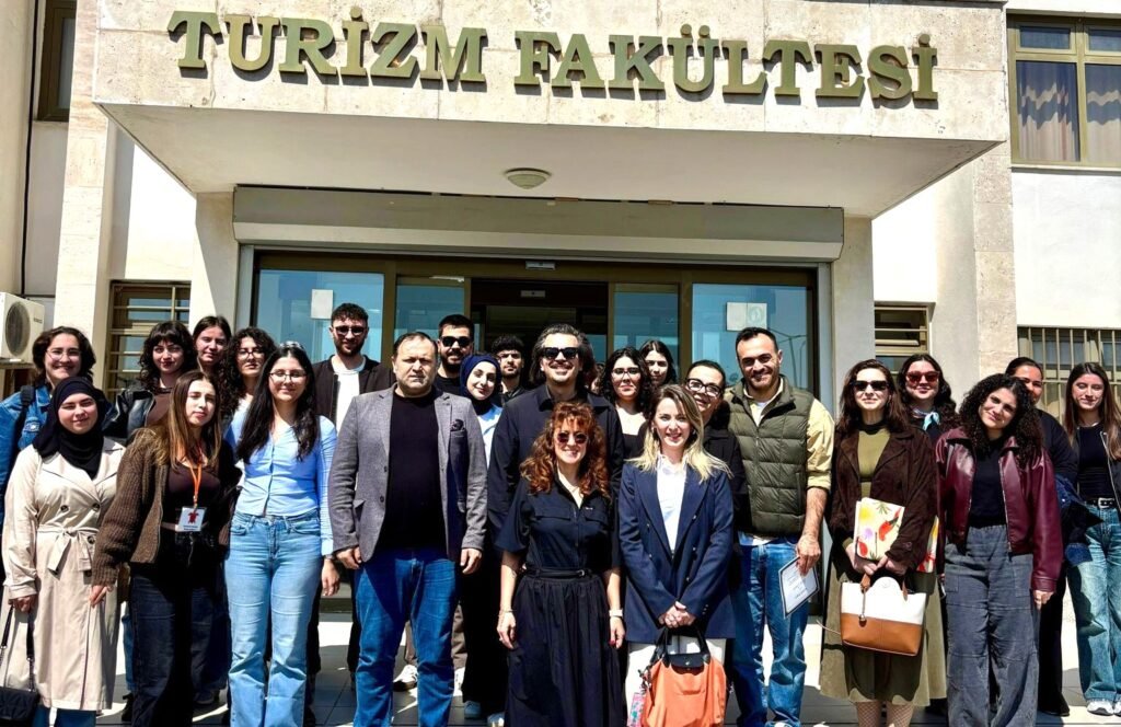 Group of students and faculty posing in front of the Turizm Fakültesi entrance.