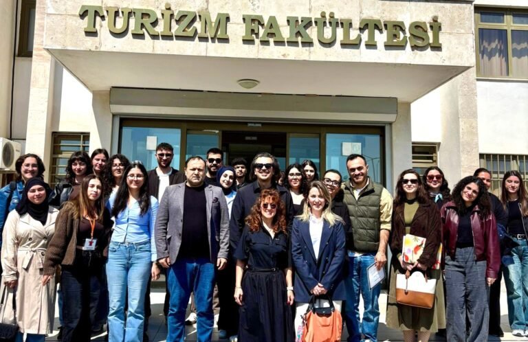 Group of students and faculty posing in front of the Turizm Fakültesi entrance.