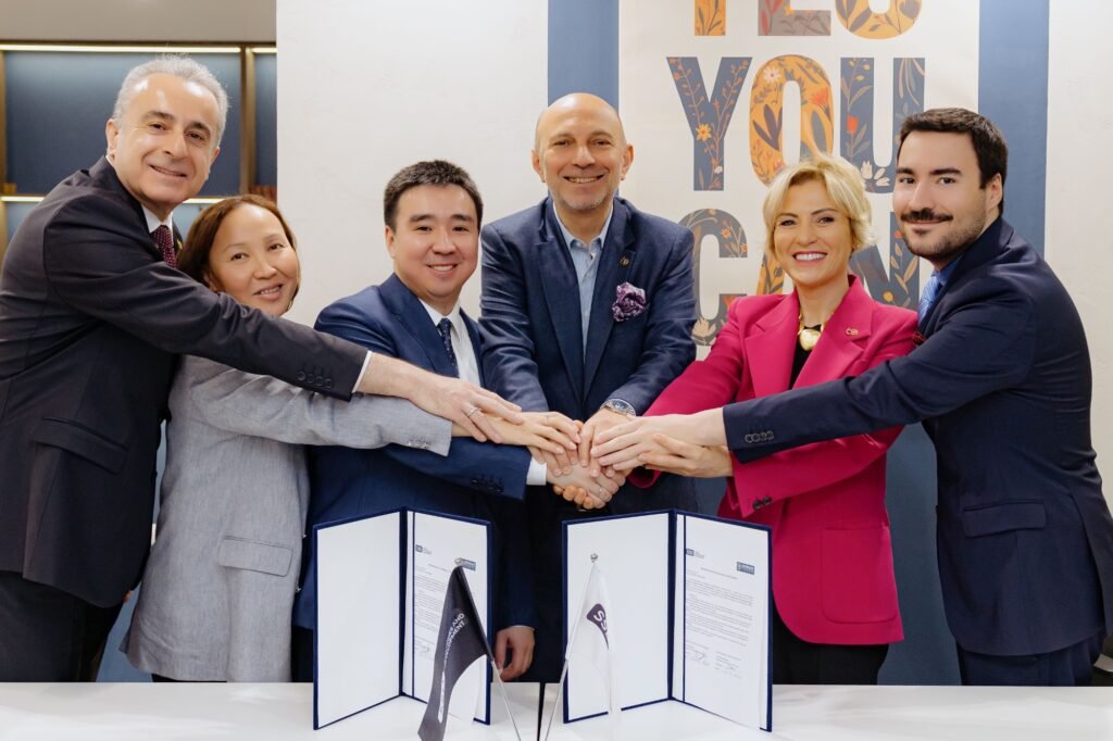 Six professionals in business attire join hands over a table with signed documents, signaling a partnership agreement.
