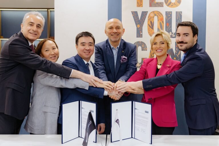 Six professionals in business attire join hands over a table with signed documents, signaling a partnership agreement.