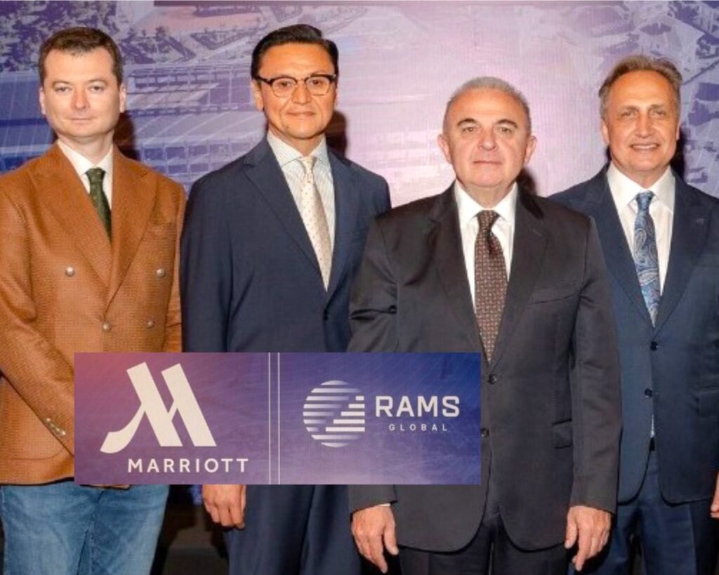Four men in suits pose for a group photo with a Marriott and RAMS Global banner backdrop.