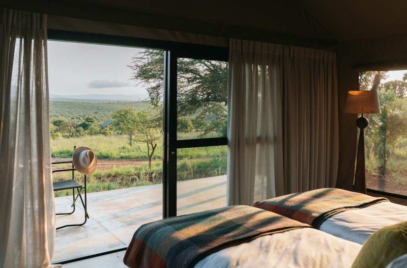 Hotel room with two beds and a view of a grassy landscape through sliding glass doors.