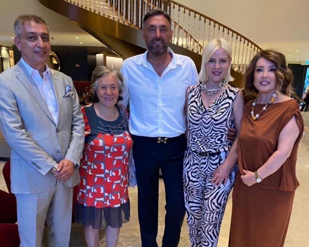 Five adults standing together in a hotel lobby, posing for a photo near a curved staircase in the background.