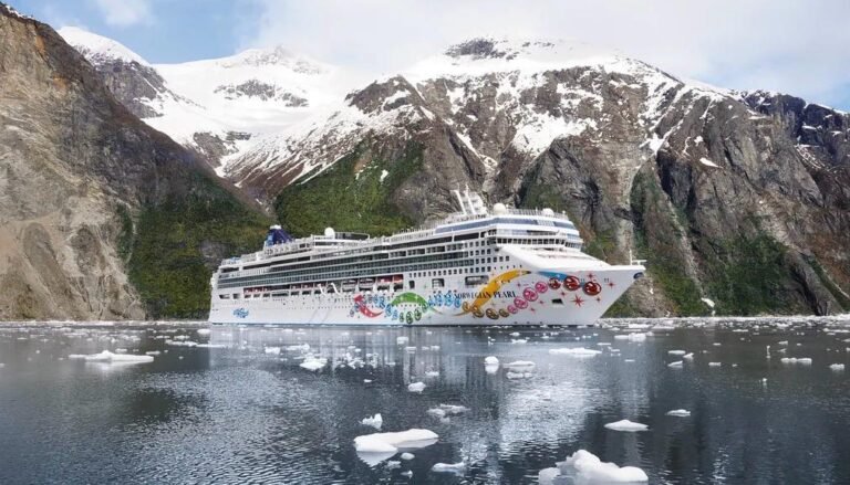 White cruise ship with colorful decorations in an icy fjord, snow-capped mountains behind.