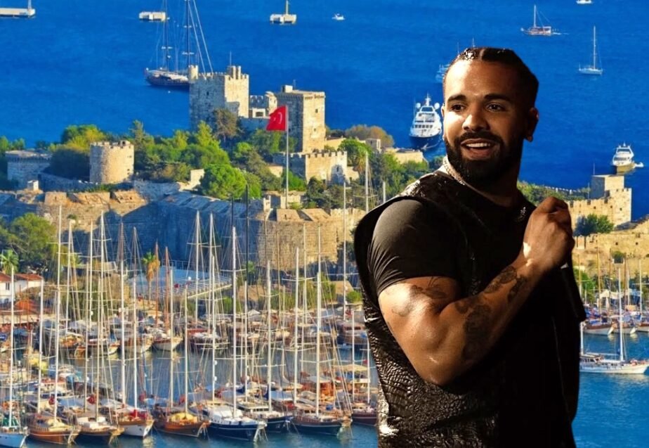 Smiling man in a black shirt posing beside a busy marina with sailboats and a historic fortress.